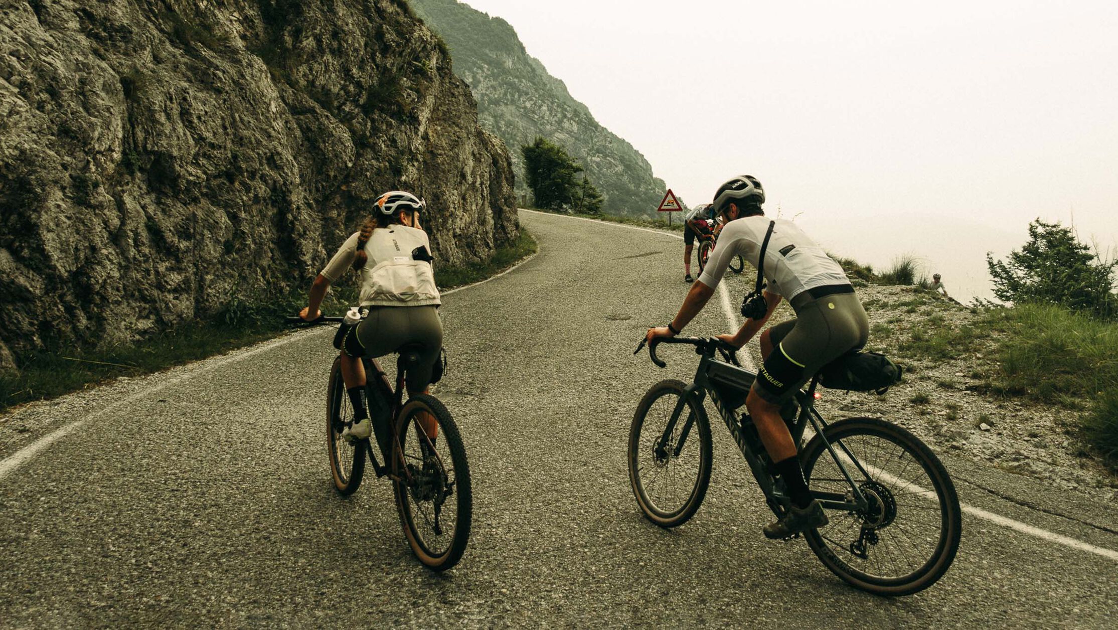 Two cyclists wearing Canyon cycling apparel while riding uphill on a mountain road, showcasing comfortable and aerodynamic gear for long-distance adventures.